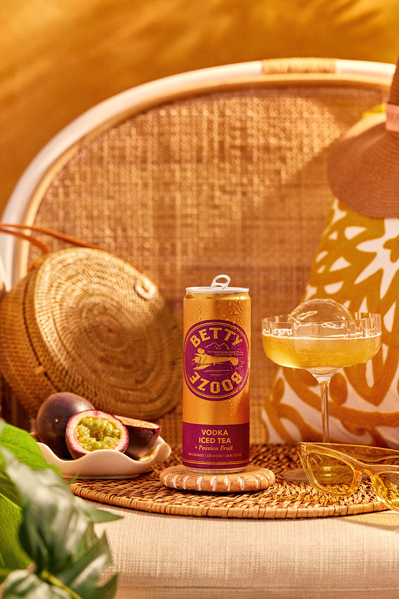 Betty Booze Vodka Iced Team + Passion Fruit Can next to a glass and passion fruit