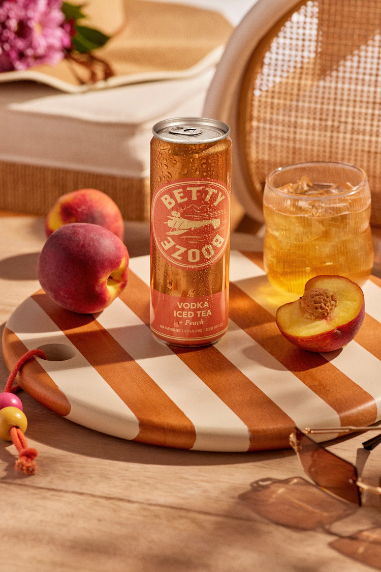Betty Booze Vodka Iced Tea + Peach Can on a table next to peaches